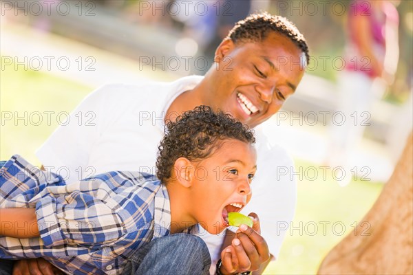 African american father and mixed-race son eating an apple in the park
