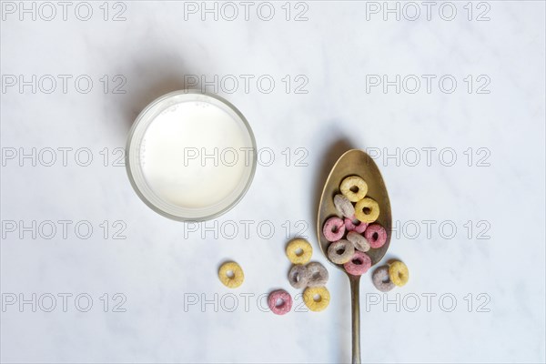 Fruit-flavoured cereal rings in spoon and glass of milk