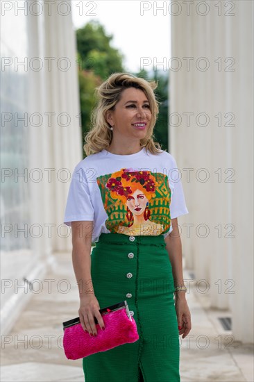 Portrait in einem Park einer huebschen Dame in ihren vierziger Jahren mit langen blonden Haaren. Sie geht auf die Kamera zu und blickt mit ueberraschte Blick zu Seite. Ein gruener langer Rock mit bedr...