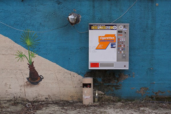 Cigarette vending machine on blue wall with wastepaper basket and gaffiti