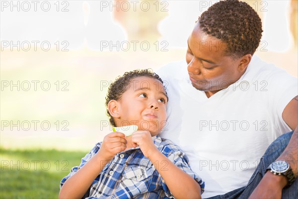 African american father and mixed-race son eating an apple in the park