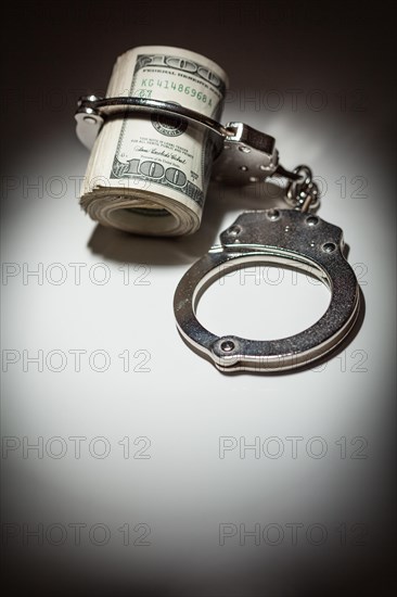 Handcuffs locked on roll of one hundred dollar bills under spotlight