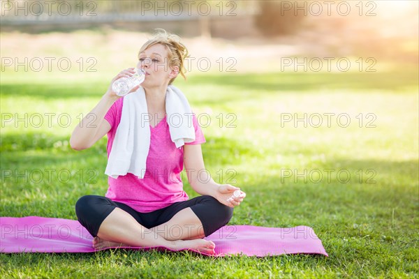 Young fit adult woman outdoors on her yoga mat with towel drinking from her water bottle