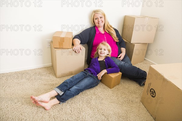 Happy young mother and daughter in empty room with moving boxes
