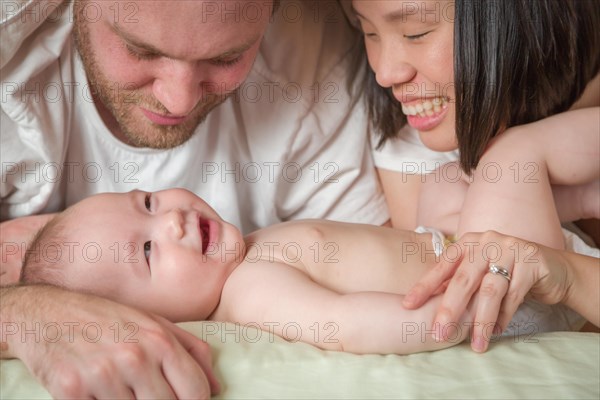 mixed-race chinese and caucasian baby boy laying in bed with his father and mother