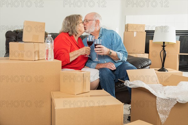 Senior adult couple toasting wine glasses surrounded by moving boxes