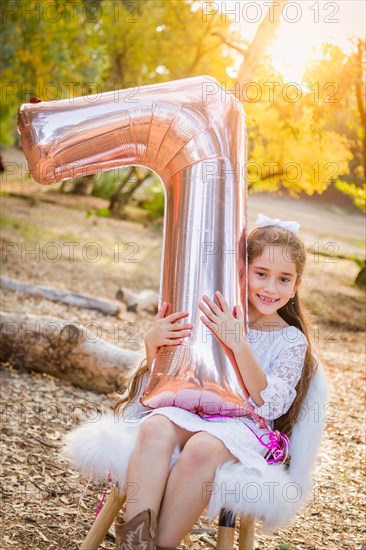 Cute young girl playing with number seven mylar balloon outdoors