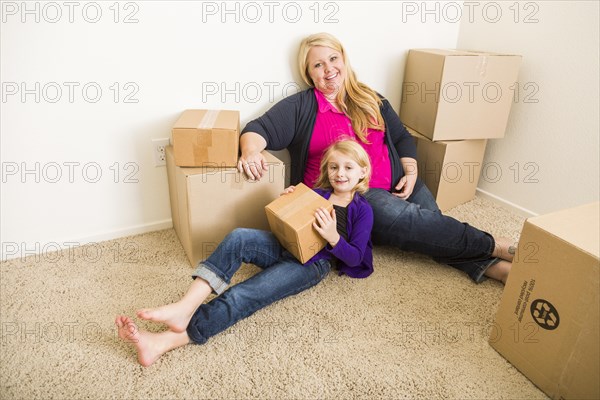Happy young mother and daughter in empty room with moving boxes
