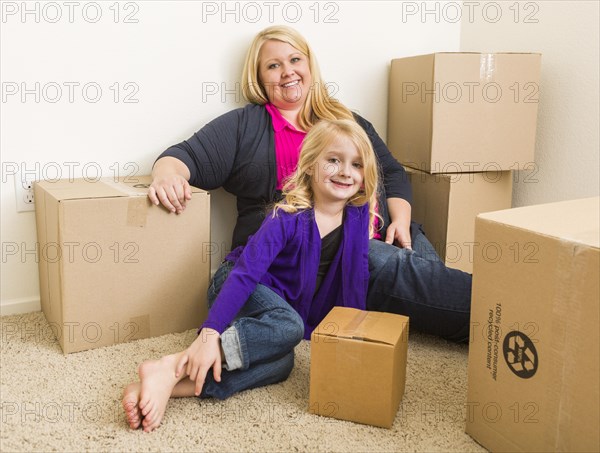 Happy young mother and daughter in empty room with moving boxes