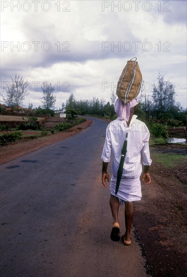 A man carrying bag over his head and an umbrella behind his shirt on the road