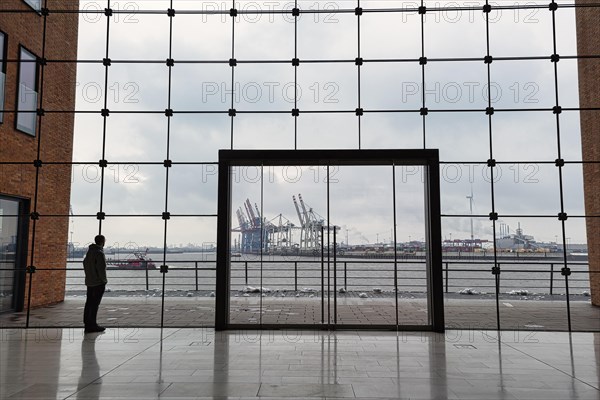 Young man standing in front of modern glass facade with large door and looking at the harbour