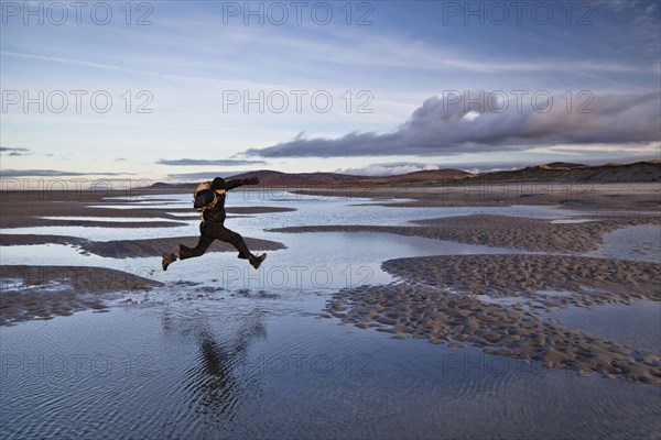 Man jumping over tidal sea puddles