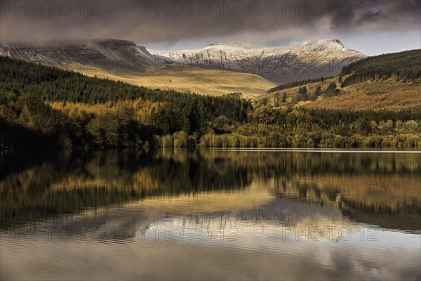 Trees and snow-capped hills reflected in the reservoir at sunrise