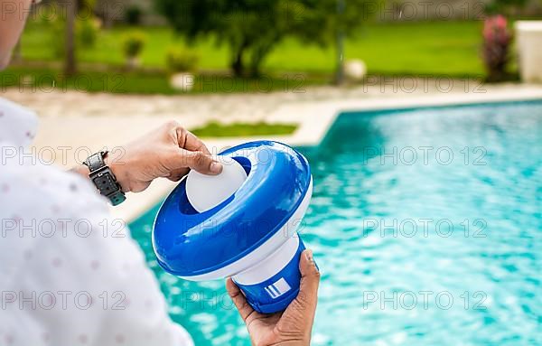 Pool float and chlorine tablets for pool maintenance. Hands holding a pool chlorine dispenser. Hand of a pool disinfection worker holding a dispenser with a chlorine tablet. Hands holding a dispenser ...