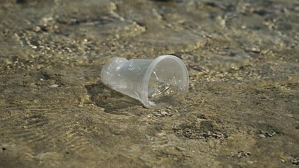 Transparent plastic cup is carried away by the wind to the sea in the coastal zone. Plastic pollution of the surf zone. Red sea