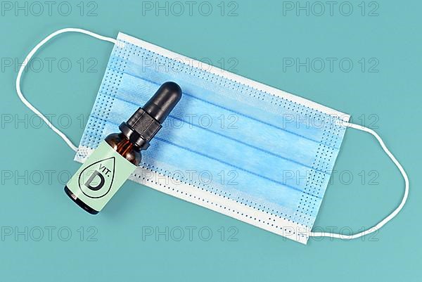 Vitamin D helping fight Corona virus illness. Concept with medical face mask and bottle with vitamin drops on blue background,