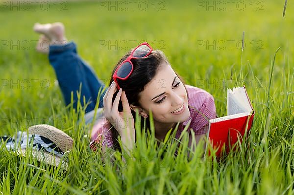 Young woman lying in meadow and reading a book,