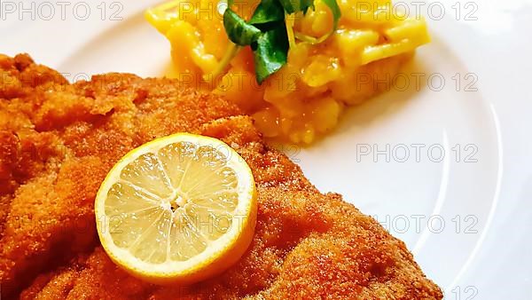Delicious golden-brown fried Wiener Schnitzel with potato salad and a slice of lemon on a white plate,