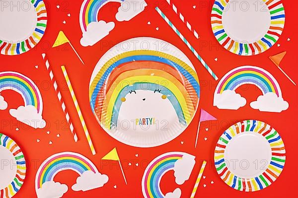 Party flat lay with colorful plates, rainbow napkins and drinking straws on red background
