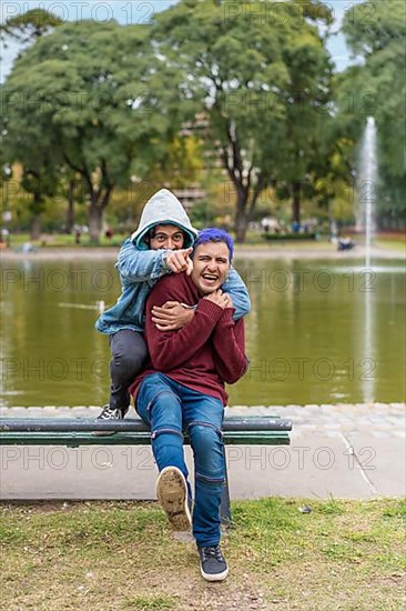 Gay Latino male couple sitting on a bench in a park laughing,