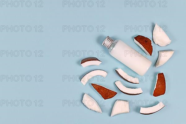 Slices of coconut fruit and bottle filled with coconut oil used for food preparation and cosmetic beauty products on blue background with copy space,