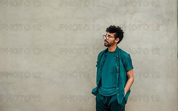 Pensive handsome man leaning on a wall looking up, worried male with hands in pocket looking up