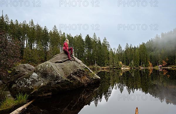 Woman in red on rocks in Glaswaldsee surrounded by forest