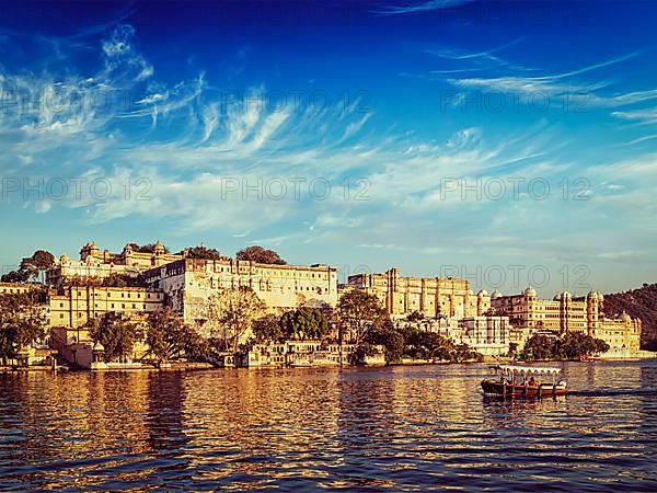 Vintage retro effect filtered hipster style image of City Palace and tourist boat on lake Pichola on sunset. Udaipur