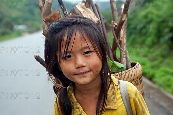 Close-up of a young Lao girl carrying firewood in a basket on her back