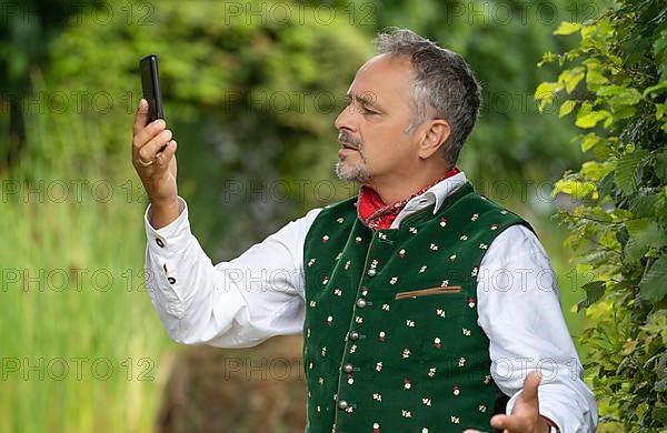 Middle-aged man in Bavarian traditional costume looking confused at his phone