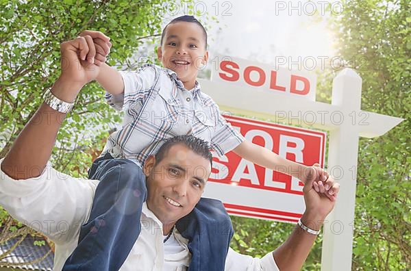Happy young hispanic father and son in front of sold for sale real estate sign