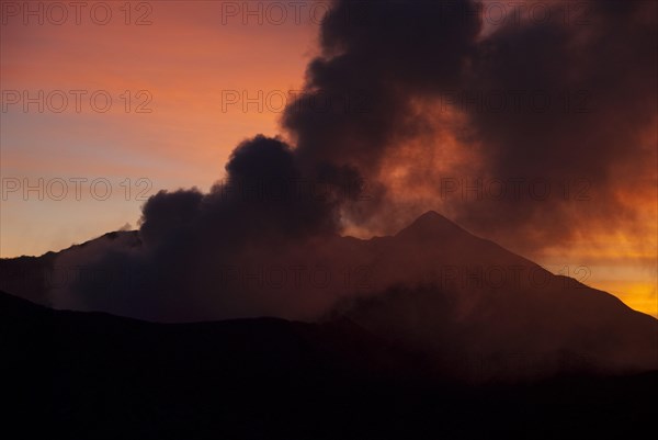 Smoke rising from volcano at sunset