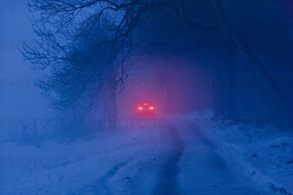 Distant brake lights of a car on a snow-covered road in freezing fog at dusk
