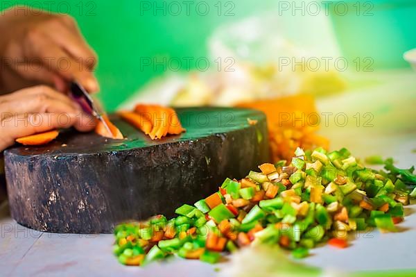 Hands cutting carrot pieces on a homemade chopper. Close up of hands chopping carrots in a wooden chopper. Concept of hands cutting vegetables in a wooden chopper