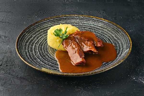 Roasted beef slices with wine sauce and mashed potato on dark background