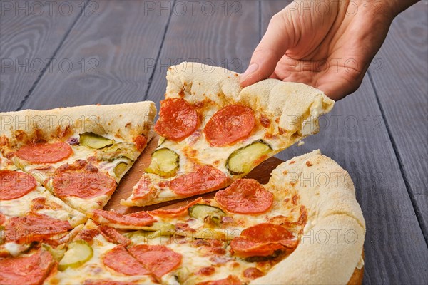 Hand taking slice of pizza pepperoni from plate