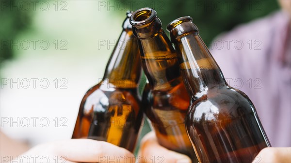 Close up friends clinking brown beer bottles
