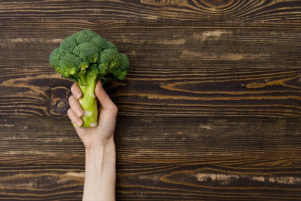 Overhead view of fresh broccoli in hands over wooden background