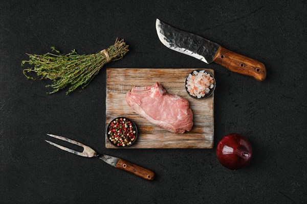 Overhead view of raw veal steak bone in with ingredients for cooking on black background