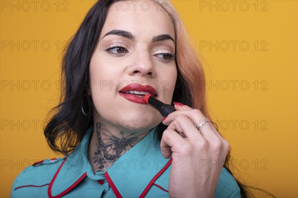 Beautiful caucasian woman applying a bright red color lipstick on her lips over yellow background