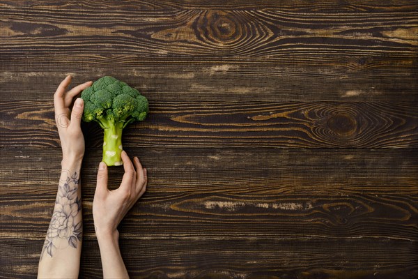 Overhead view of fresh broccoli in hands over wooden background