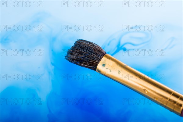 Watercolor paint dissolving in water as painting brush touches water