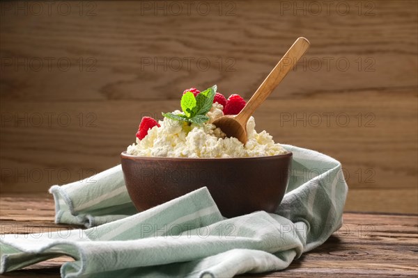 Fresh cottage cheese with raspberries and wooden spoon in clayware on wooden table