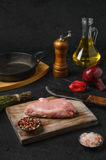 Raw veal steak bone in with ingredients for cooking on black background