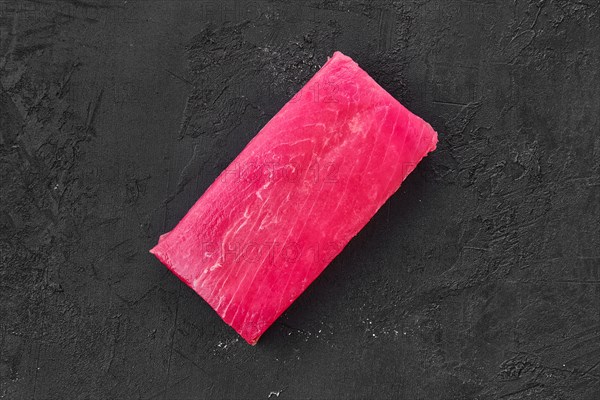 Raw frozen tuna fillet on black background