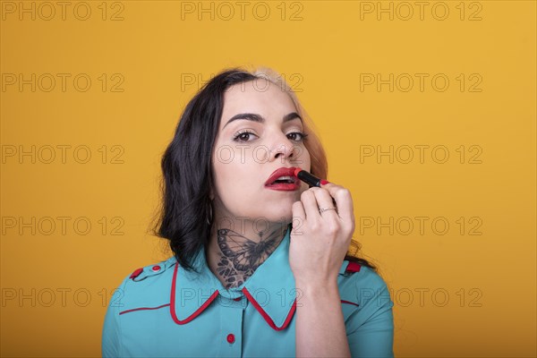 Beautiful caucasian woman applying a bright red color lipstick on her lips over yellow background