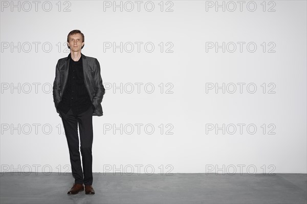 Man in wool jacket standing near white concrete wall with hands in pocket