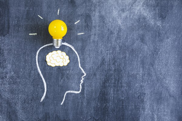 Yellow light bulb paper cutout brain outline face made with chalk blackboard. Resolution and high quality beautiful photo