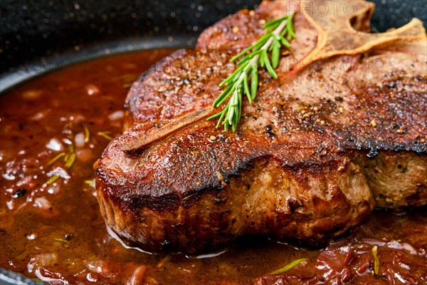 Closeup view of Porterhouse steak in wine sauce in frying pan