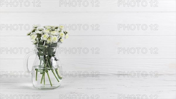Chrysanthemum flowers inside glass jug against white wooden background